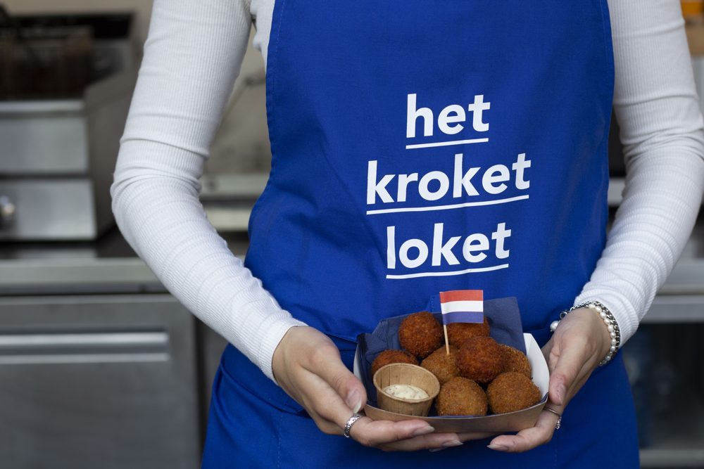 Medewerker in blauw schort presenteert bitterballen